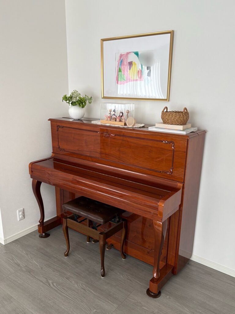 ピアノの写真。ピアノの上には額縁、花瓶、バスケット、ひな人形が飾ってある